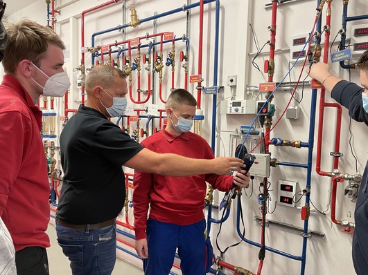 Sebastian Bien, Resideo-Außendienstmitarbeiter, führt gemeinsam mit angehenden Anlagenmechanikern Messungen an Abgleichventilen durch.