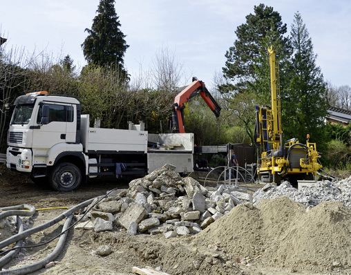 „Baustelle mit einem weißen LKW, einem orangefarbenen Kran und einer gelben Bohrmaschine, umgeben von Schutt und Kieshaufen. Die Szene illustriert moderne Installationstechniken für die SHK-Branche, einschließlich innovativer Ansätze in der Wärmeverteilung und Wasserversorgung. - © Bild: photo 5000 - stock.adobe.com