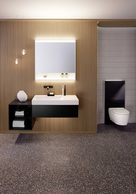 Alt-Text: „Modernes Badezimmer mit Holzverkleidung, beleuchtetem Spiegel, schwarzem Waschbecken, offenem Regal mit Handtüchern und wandhängendem WC für energieeffiziente Haustechniklösungen in der SHK-Branche. - © Bild: Geberit