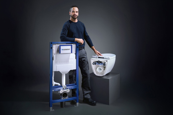„Fachkraft präsentiert modernes Vorwandelement mit WC-Keramik vor schwarzem Hintergrund, symbolisiert innovative Lösungen in der Sanitärinstallationstechnik. - © Geberit