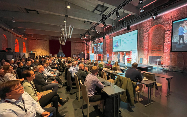 „Fachpublikum bei einer Konferenz zum Thema Sanitär-, Heizungs- und Klimatechnik in einem Raum mit moderner Präsentationstechnik; im Hintergrund rote Backsteinwände und diffuse Deckenbeleuchtung. - © Bild: Tim Geßler / Gentner