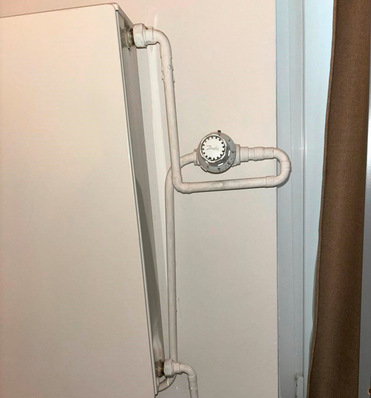 „Weißer Heizkörper mit sichtbaren Rohrleitungen und rundem Messgerät, installiert an einer Wand, veranschaulicht moderne Installationstechniken in der Heizungsbranche. - © Bild: Frank Wies