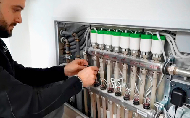 Gerne! Hier ein barrierefreier, optimierter und themenrelevanter Alt-Text für das Bild in Ihrem Fachkontext: Alt-Text: „Ein SHK-Fachmann justiert Steuerungsventile und elektrische Anschlüsse an einem modernen Heizungs- und Trinkwasserverteiler innerhalb einer Gebäudewand. Die komplexe Installation zeigt Komponenten der Sanitär-, Heizungs- und Klimatechnik zur effizienten Wärmeverteilung im Objektbau.“ Wenn Sie eine noch spezifischere Ausrichtung wünschen (z.B. Fokus auf bestimmte Technologie, Innovation oder die Anwendung), passen wir den Text gerne weiter an. - © Bild: Blossom-IC