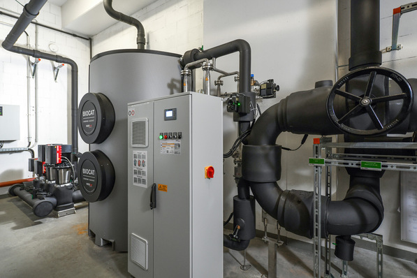 Optimierter, spezifischer Alt-Text: „Technikraum mit modernen Pufferspeichern, Heizungsrohren und digitaler Steuerungseinheit für effiziente Heizung, Warmwasserbereitung und zentrale Gebäudeautomation in einer Großimmobilie.“. - © Watercryst Wassertechnik / Petra Schramboehmer