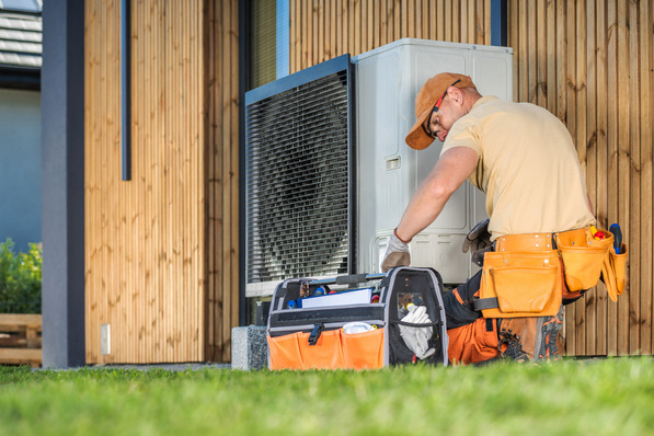 HVAC worker working on a modern heat pump outside a house.